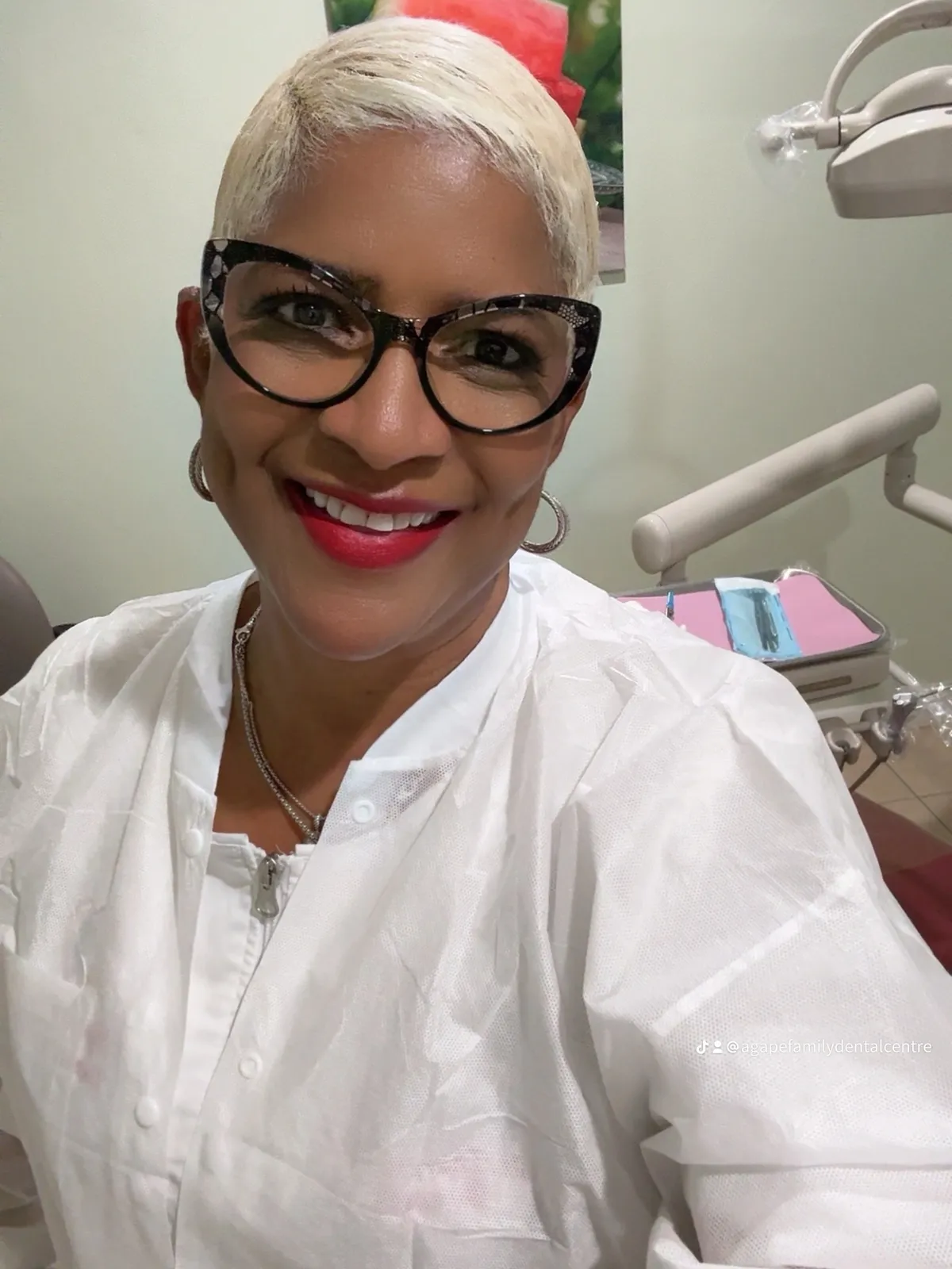 A woman with glasses and white shirt sitting in front of a dentist chair.