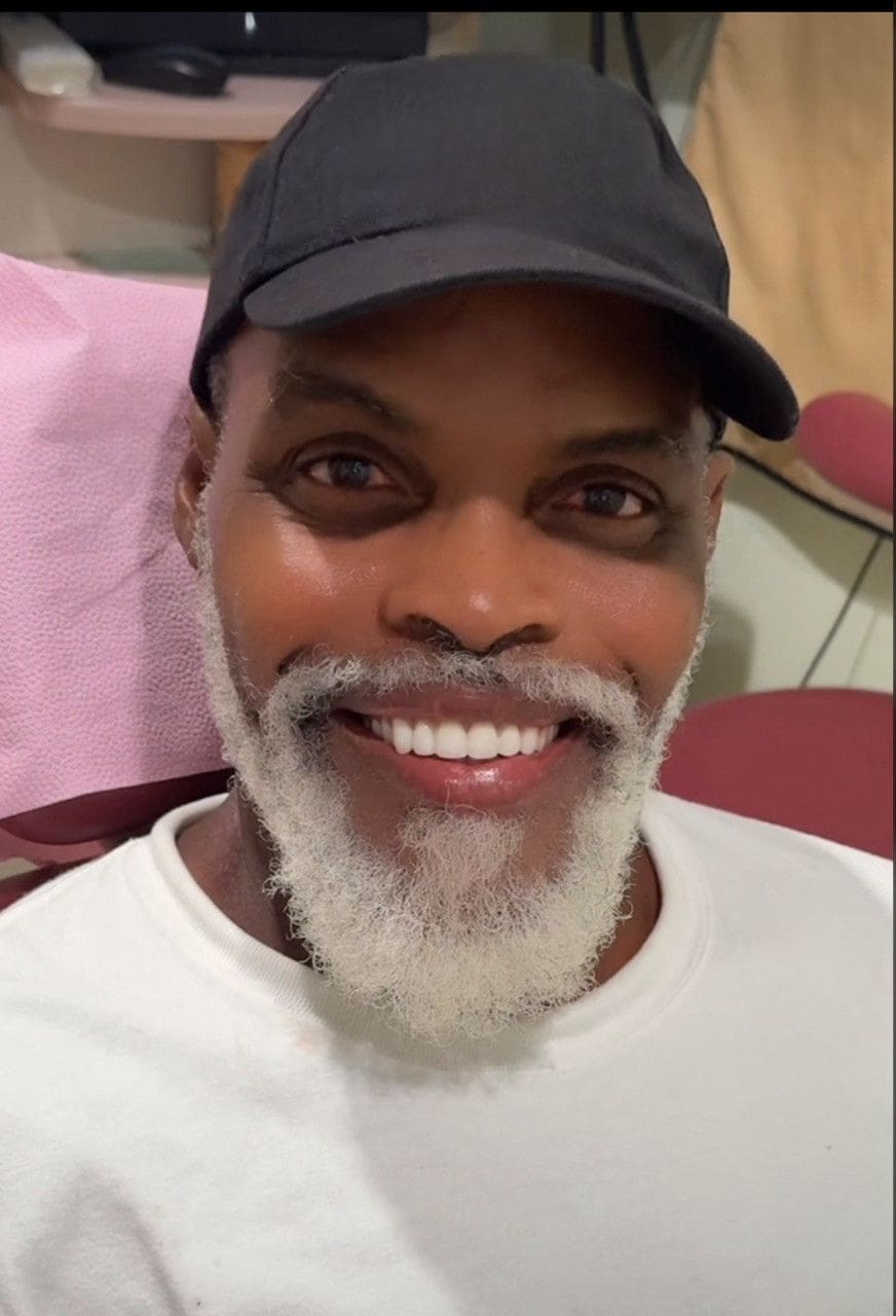 A man with white beard and hat smiling for the camera.