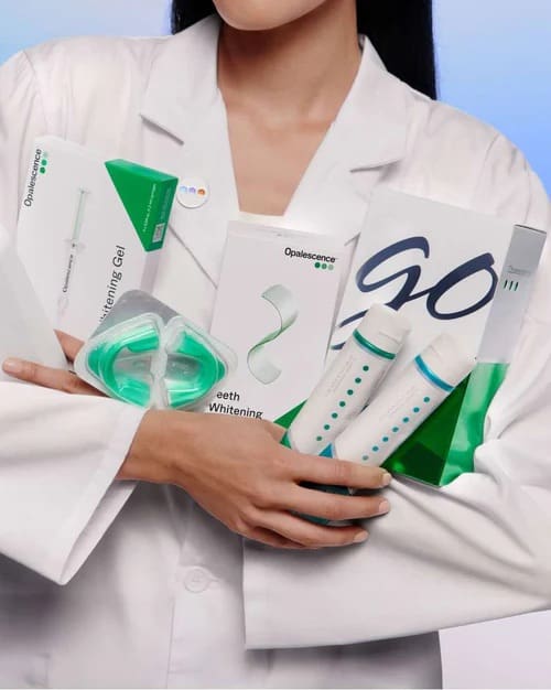 Person holding dental whitening products in lab coat.